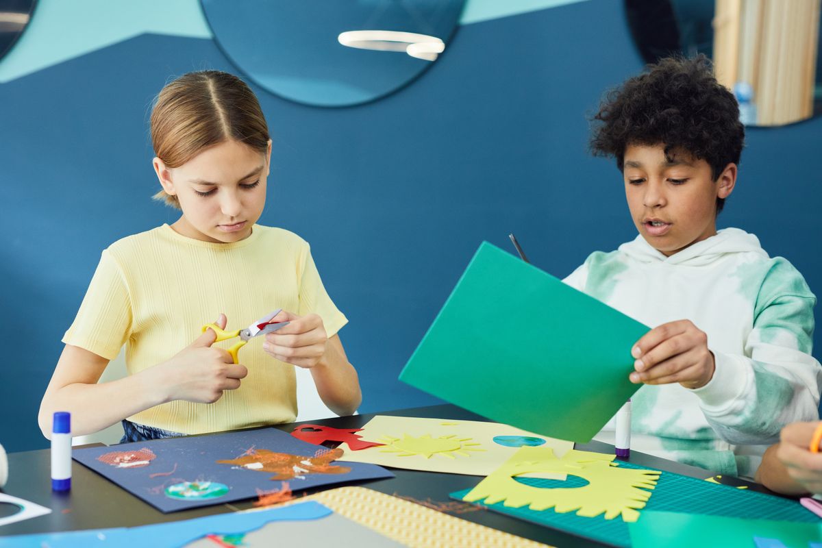 子供が机で色紙とハサミで工作をする様子